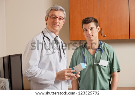 Portrait of mature male doctor holding medicine box while standing with technician