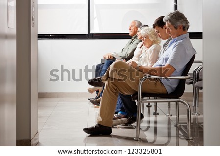 Row Of Multiethnic People Sitting Side By Side While Waiting For Doctor In Hospital Lobby