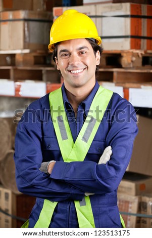 Portrait of a confident young foreman in uniform with arms crossed at warehouse