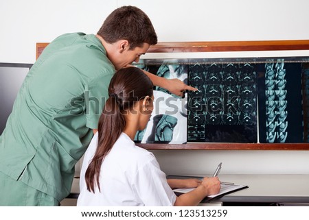 Male medical technician pointing at MRI x-ray while female jotting down notes on paper