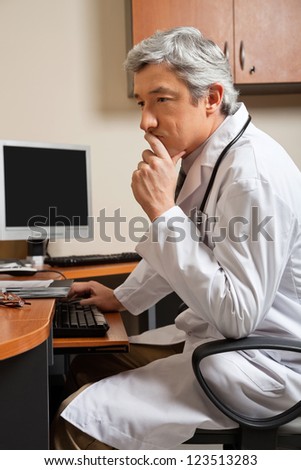 Pensive mature male doctor sitting at computer desk in clinic