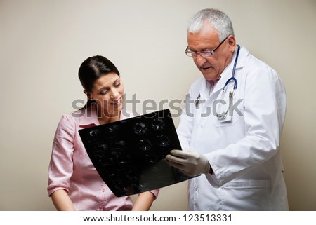 Senior male radiologist and female patient looking at x-ray against colored background