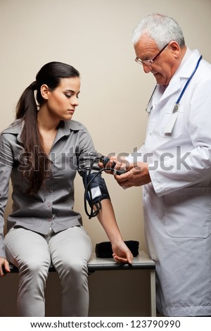 Senior male doctor taking young woman\'s blood pressure