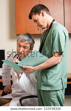 Male technician showing patient\'s report to mature doctor at clinic