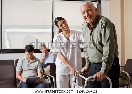 Portrait of senior man being assisted by female nurse to walk Zimmer frame with people sitting in background Portrait of senior man being assisted by female nurse to walk Zimmer frame with people sitting in background