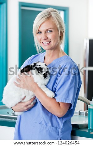 Portrait of young female veterinarian doctor carrying a rabbit at medical clinic