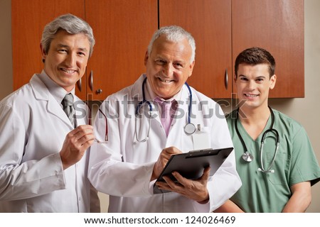 Portrait of happy senior male doctor writing on clipboard while standing with colleagues