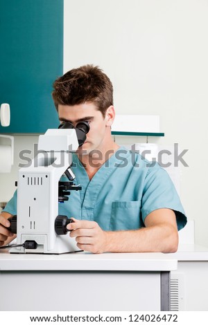 Young male researcher using microscope in hospital laboratory