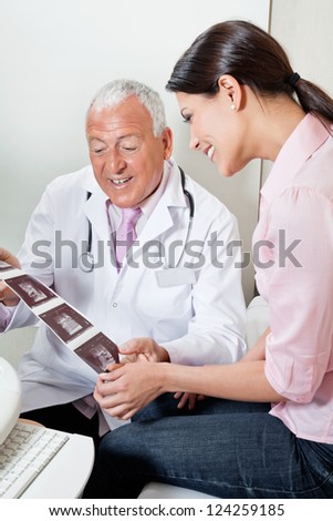 Senior male radiologist showing ultrasound print to mid adult female patient at clinic