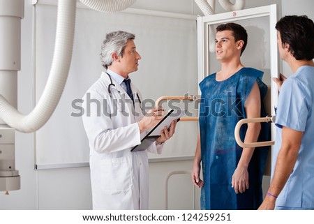 Mature radiologist and technician conducting x-ray on young male patient
