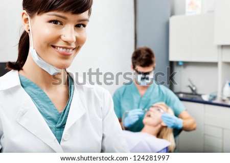 Portrait of smiling female assistant with dentist working in the background