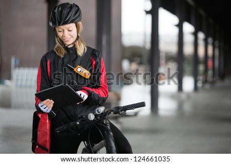 Young female cyclist in protective gear with courier bag using digital tablet