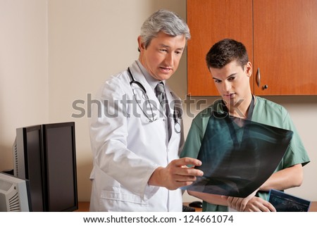 Mature doctor and male technician reviewing shoulder x-ray together at clinic