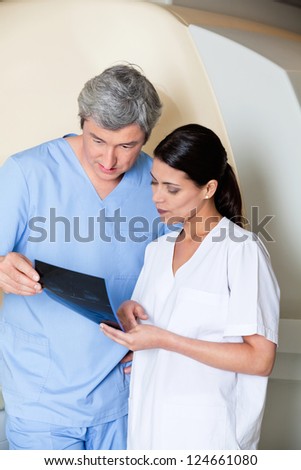 Multiethnic radiologic technicians looking at x-ray while standing by MRI scan machine
