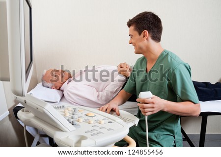 Young male radiologic technician smiling while looking at senior patient