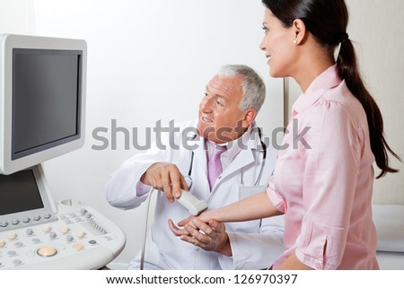 Senior male radiologist looking at monitor while scanning female patient\'s hand at clinic