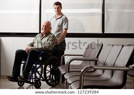 Portrait of young man with his grandfather on wheelchair in hospital lobby