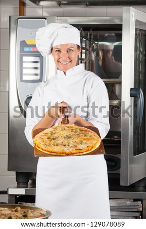 Portrait of confident female chef presenting pizza at commercial kitchen