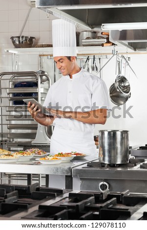 Happy male chef using digital tablet with pasta dishes at commercial kitchen counter