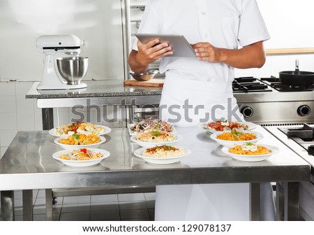 Midsection of male chef using digital computer with pasta dishes on kitchen counter