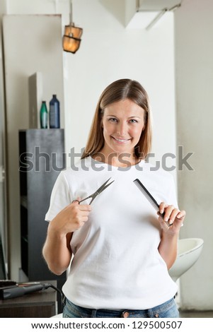 Portrait of beautiful hairdresser holding comb and scissors in beauty parlor