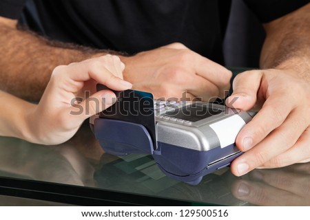 Female client\'s hand swiping credit card through terminal at salon counter