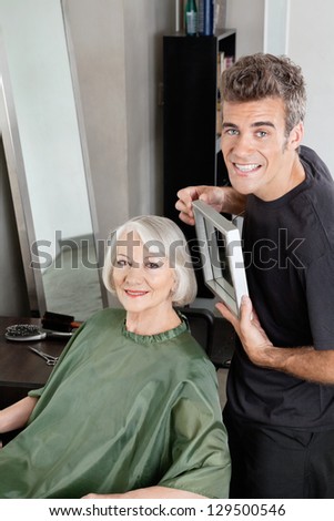 Portrait of happy customer with hairdresser holding mirror in beauty salon
