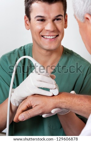 Happy young male radiologic technician scanning male patient\'s hand