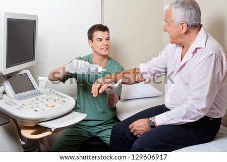 Young male radiologic technician looking at patient while putting gel on his hand