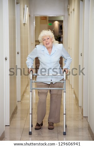 Full length portrait of an elderly woman with walker standing in hospital corridor