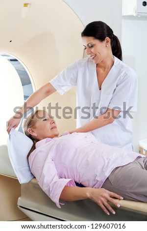 Radiologic technician smiling while preparing a mature female patient for a CT scan