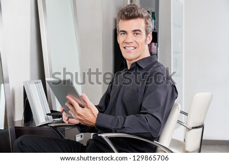 Portrait of male customer with digital tablet sitting at hair salon