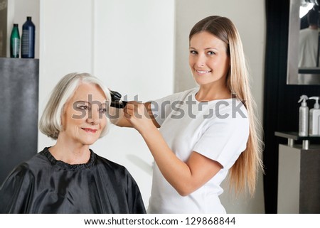 Portrait of female hairdresser with straightener ironing customer\'s hair at salon