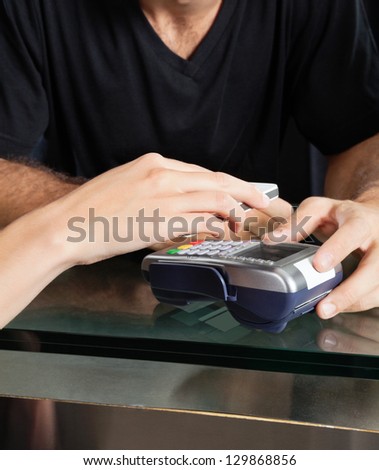 Female Customer Paying With Mobilephone Over Electronic Reader At Salon Counter
