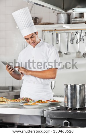 Male chef using digital tablet with pasta dishes at commercial kitchen counter