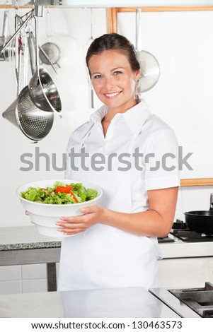 Portrait of happy female chef holding bowl of salad by industrial kitchen counter