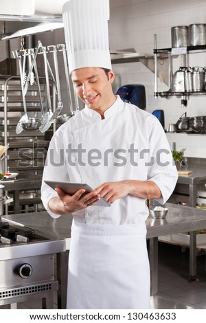 Young male chef using digital standing in restaurant kitchen