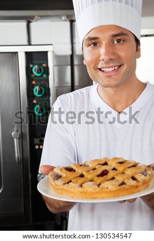 Portrait of happy young chef presenting sweet dish in industrial kitchen