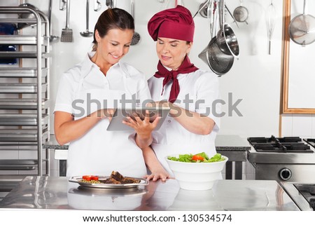 Happy female chefs with digital tablet discussing in commercial kitchen