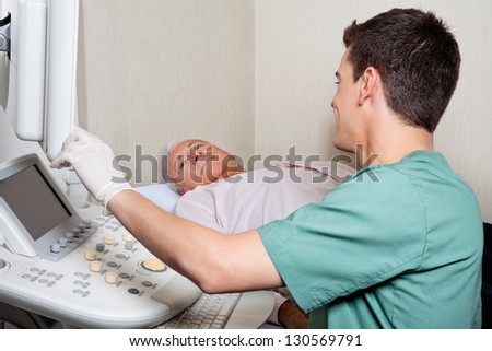 Young male technician showing ultrasound machine\'s monitor to senior patient