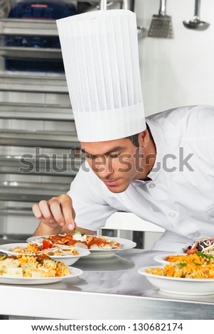 Young male chef garnishing pasta dishes at commercial kitchen counter