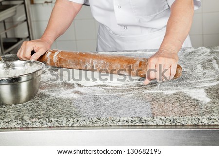 Midsection of female chef rolling dough at kitchen counter