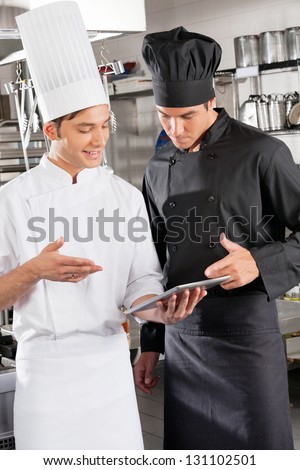 Male chefs with digital tablet discussing in restaurant kitchen