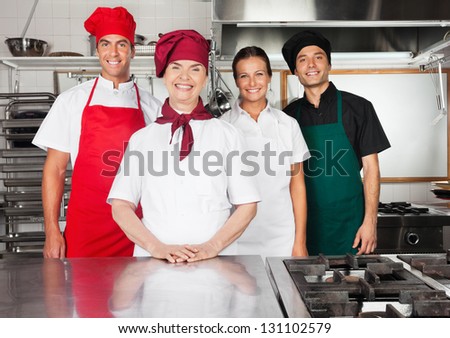 Portrait of happy female mature chef with colleagues in commercial kitchen