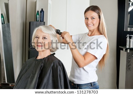 Portrait of female hairdresser ironing senior woman\'s hair in salon