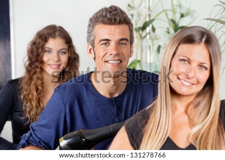 Portrait of happy male hairstylist with female colleagues at beauty parlor