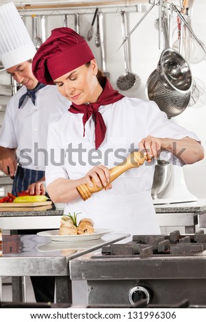 Female chef seasoning salmon roll with colleague in background