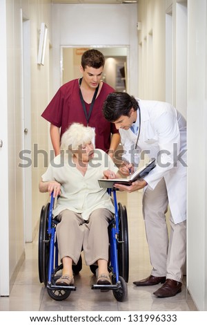 Doctor communicating with disabled senior female patient in hospital corridor