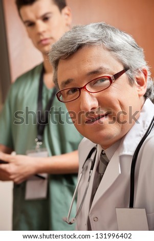Portrait of mature doctor with male technician standing in background