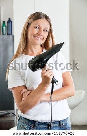 Portrait of female hairstylist with hair dryer at beauty salon